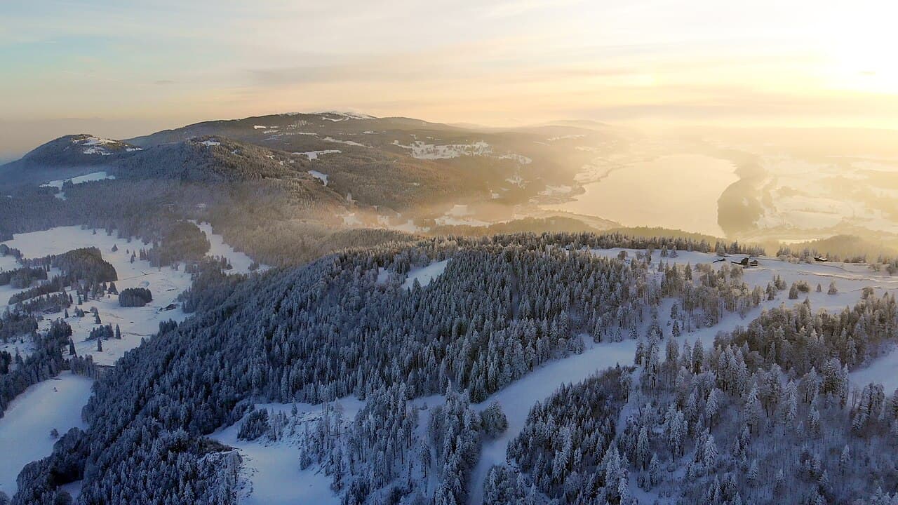 Reliefs et forêts enneigés de la Dent de Vaulion, avec le lac de Joux à l’arrière-plan au coucher du soleil
