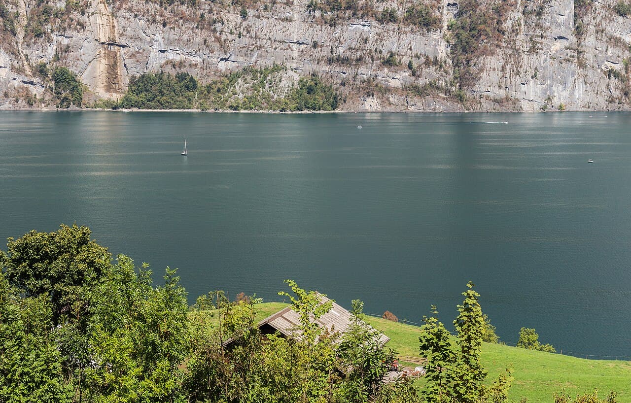 Voiliers sur le Walensee au pied de versants rocheux, avec un chalet et de la végétation au premier plan