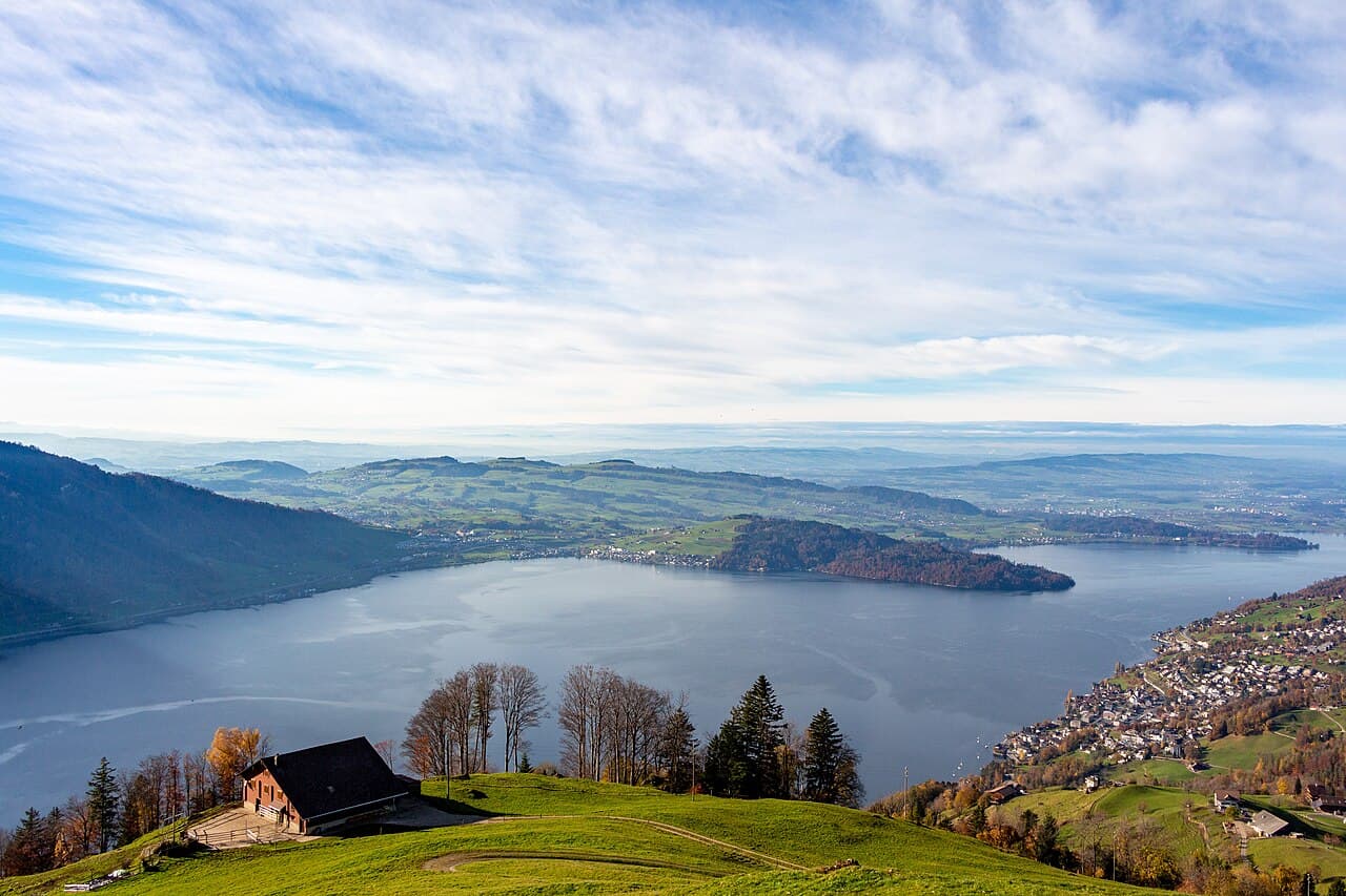 Vue du lac de Zoug depuis les hauteurs, avec une ferme au premier plan et la presqu’île de Chiemen